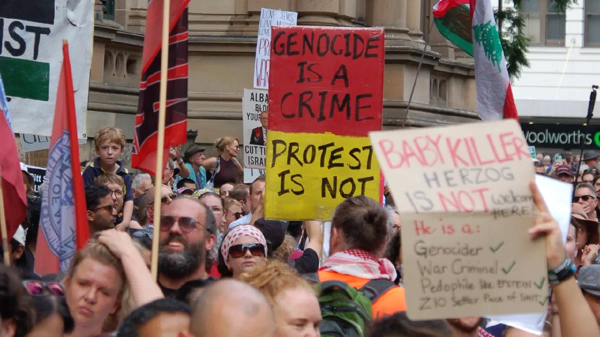 Protestors at the Herzog rally in Sydney hold up placards. One reads ‘Genocide is a crime. Protest is not.ʼ.