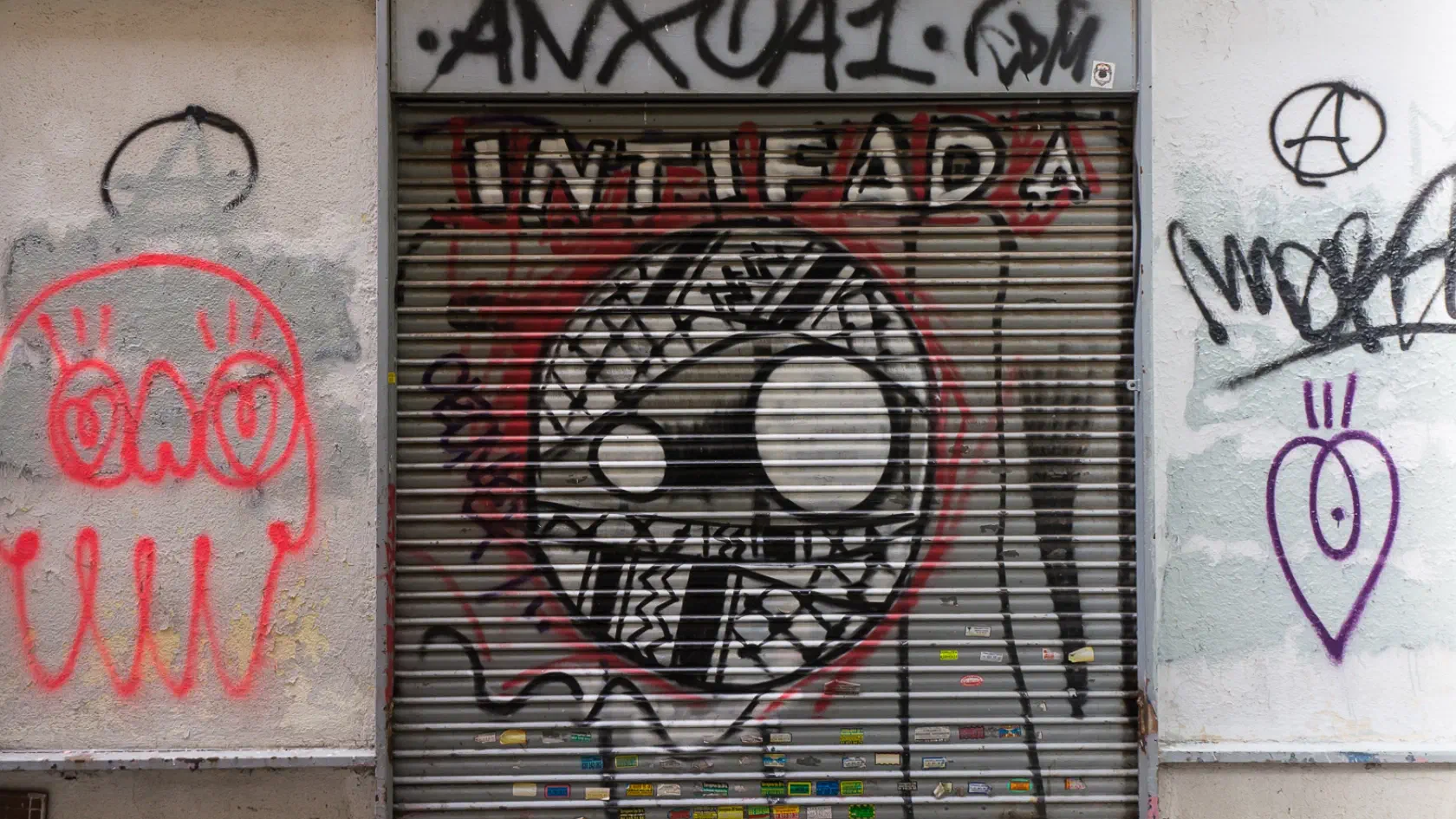 Graffiti on a shutter door of a stylised face wrapped in a keffiyeh with the word ‘Intifadaʼ.