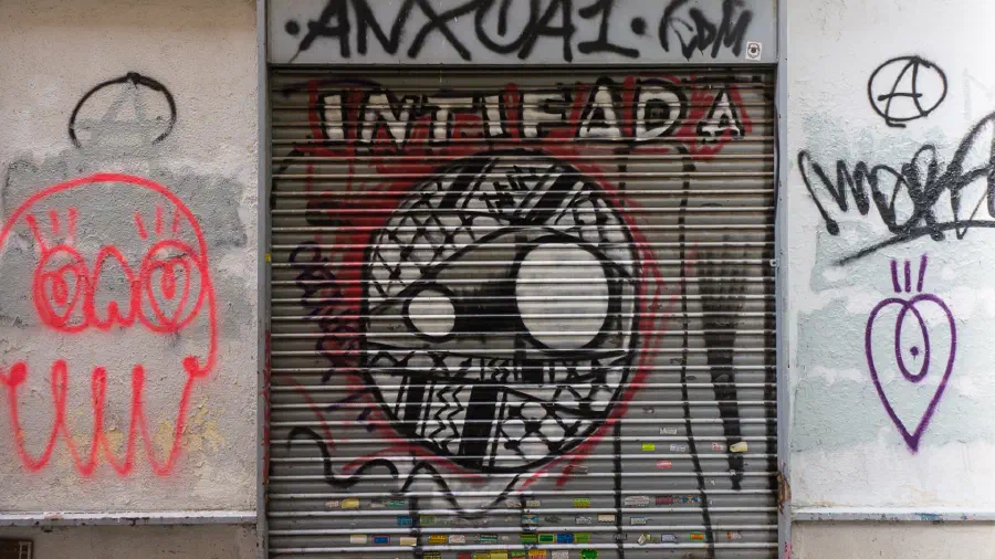 Graffiti on a shutter door of a stylised face wrapped in a keffiyeh with the word ‘Intifadaʼ.