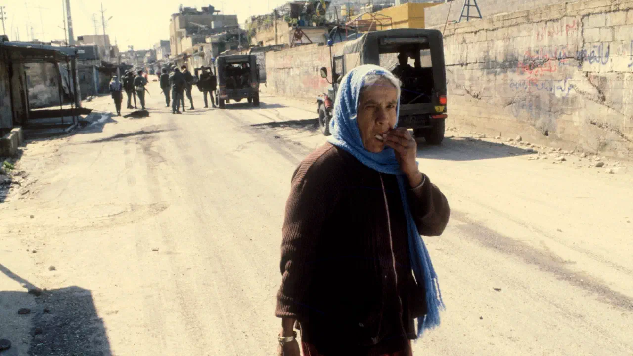 A Palestinian woman walks down a Gaza street while military figures emerge from trucks behind her.