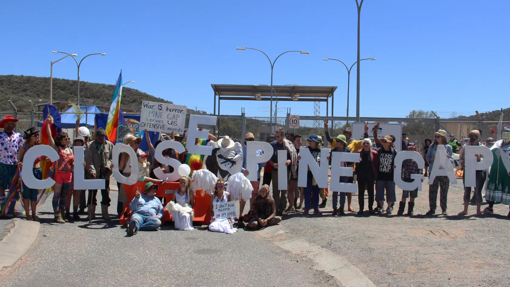 Protestors hold up large cutout letters to spell the words ‘Close Pine Gapʼ outside the gates of the Pine Gap facility.