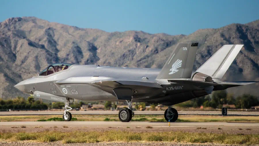 A Lockheed Martin F-35A jet sits in front of mountains in a desert landscape.