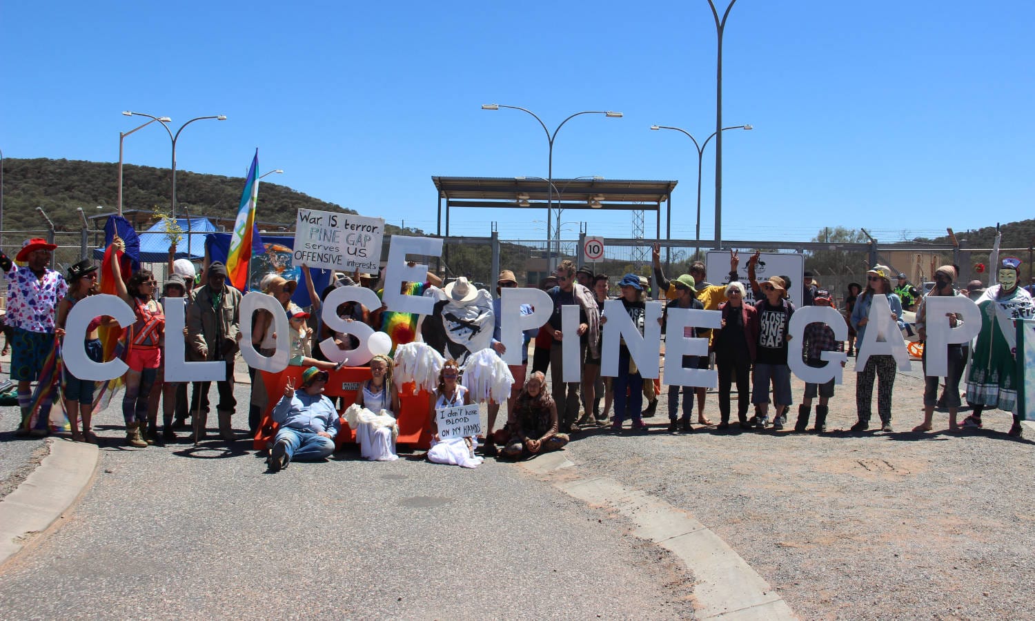 Protestors hold up large cutout letters to create the words 'Close Pine Gap' outside Pine Gap